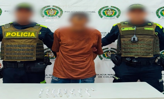 Dos funcionarios policiales con un ciudadano capturado frente a pendón institucional 