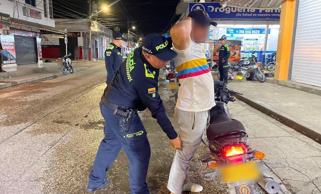 Tres funcionarios policiales, uno realizando registro a persona a un ciudadano al lado de una motocicleta