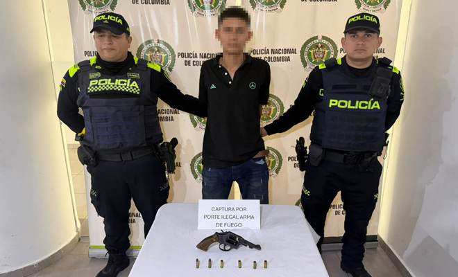 dos polic&iacute;as con un capturado y un revolver con munici&oacute;n sobre la mesa.