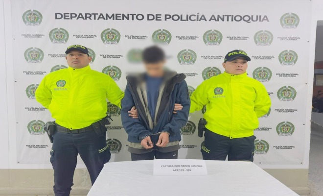 Dos policías con chaqueta verde de SIJIN custodian a un capturado