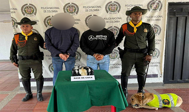 Dos polic&iacute;as,  dos personas capturadas , una bolsa de estupefaciente encima de una mesa y un perro.