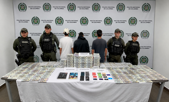 Se observa cuatro uniformados de la Polic&iacute;a Nacional con tres personas capturadas una mesa que tiene sobre ella m&aacute;s de 7 millones en papel moneda extrajera cuatro celulares y dos libretas de anotaciones