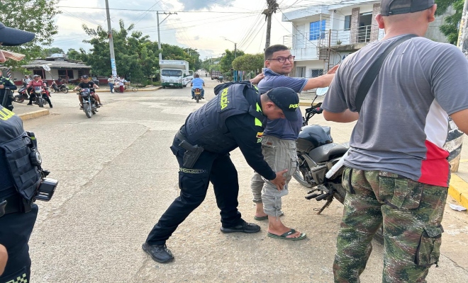 un policía registrando a dos ciudadanos y un policía prestando seguridad  