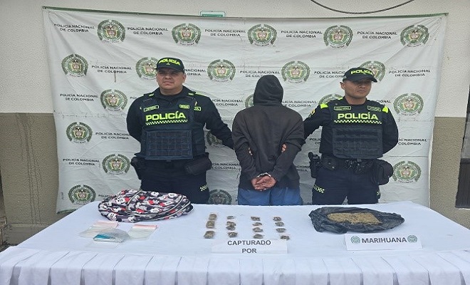 Dos policias junto a un hombre de camisa negra de espalda con capota y marihuana en una mesa