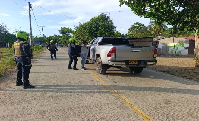 un policía registrando a un ciudadano en un carro y dos policías prestando seguridad 
