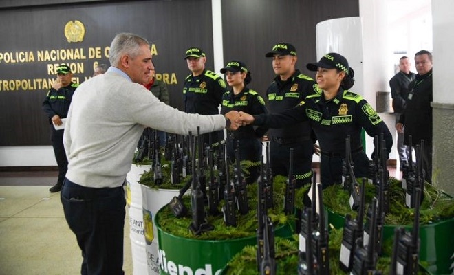 Gobernador del Departamento de Antioquia saludando a una funcionaria de la Polic&iacute;a Nacional, acompa&ntilde;ados de 4 miembros uniformados y dos no uniformados de la instituci&oacute;n, recibiendo 20 radios de comunicaci&oacute;n para fortalecer la seguridad ciudadana.