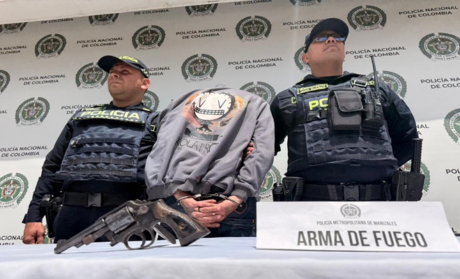 dos policías un capturado, arma de fuego incautada, mesa y un letrero 