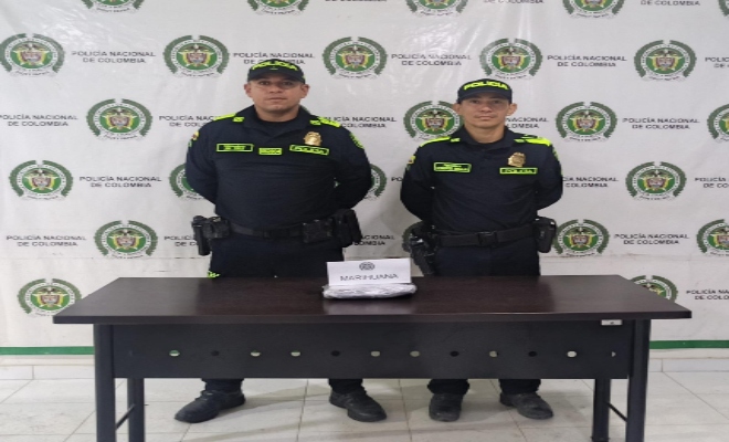Dos policías y una bolsa de marihuana incautada en una mesa.