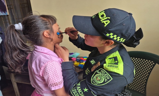 una funcionaria policial, pintando la carita a una niña de espaldas 