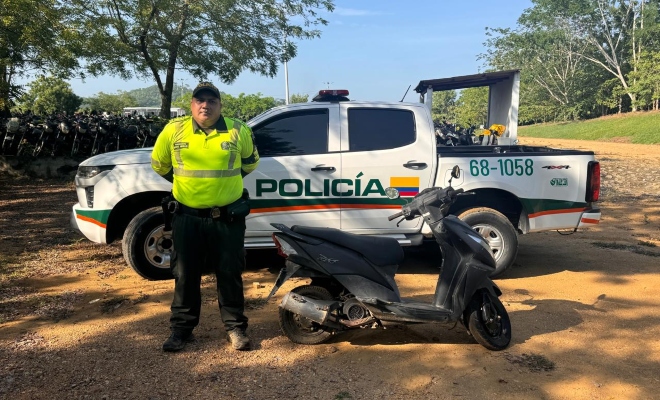 Funcionario policial de transito y transporte junto a una motocicleta recuperada en espacio abierto detrás de este una camioneta de la Policía Nacional