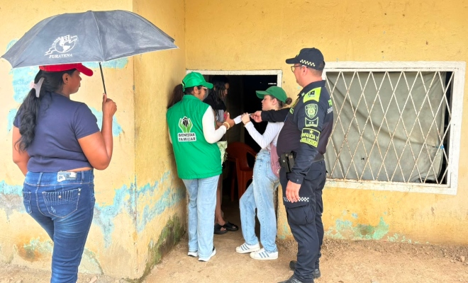 Funcionario policial junto a tres funcionarias del ICBF realizando actividad puerta a puerta en una cas color amarillo