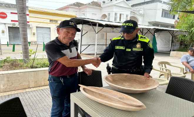 un uniformado con un ciudadano en el parque principal mostrándole las artesanía hecha por el ciudadano   