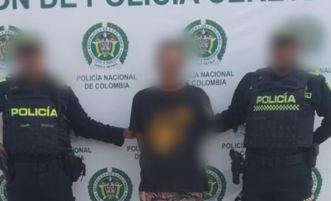 Dos funcionarios policiales con un ciudadano capturado frente a pendón institucional 
