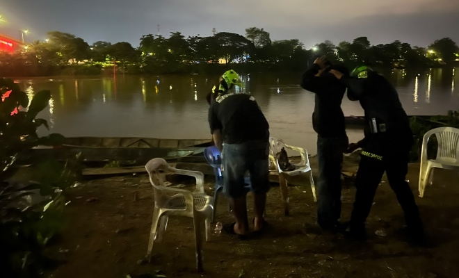 Dos funcionarios policiales realizando registro a persona a dos ciudadanos en establecimientos públicos a orillas del rio 