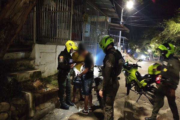 Un Policías practicando registro a dos ciudadanos, dos Policías prestando seguridad