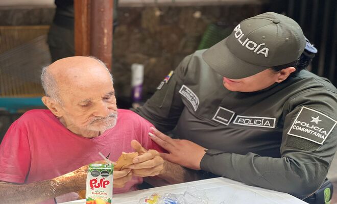 Uniformada de la policía comunitaria acompaña a un adulto mayor durante una actividad de apoyo social.