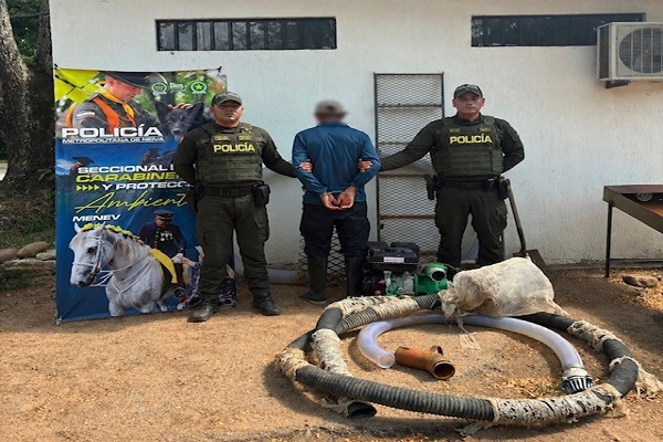 Dos polic&iacute;as custodian a un hombre capturado junto a una m&aacute;quina incautada