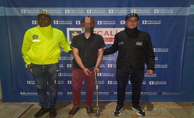 Una persona de sexo masculino capturada por el delito de homicidio agravado, acompañado de un uniformado de la Policia Nacional y un funcionario del CTI al costado brindando seguridad.
