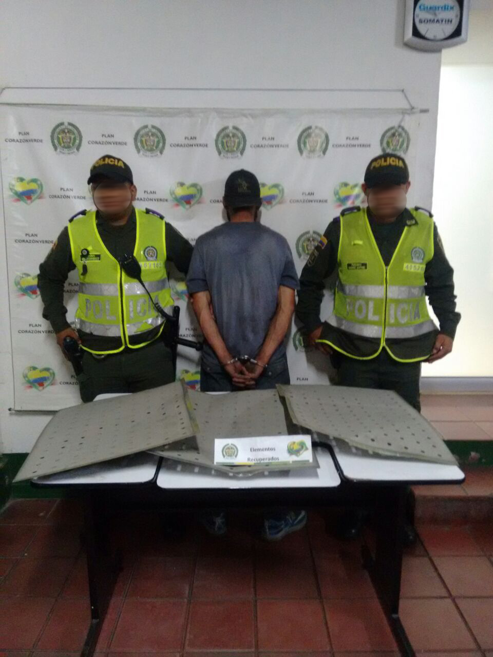 Dos policías custodian un hombre capturado con paneles hurtados en un puente de Medellín