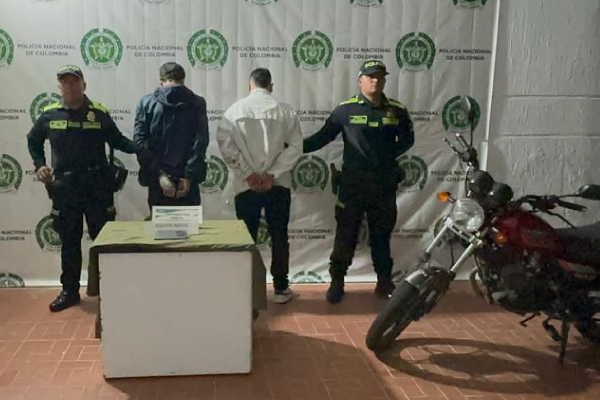 Dos hombres capturados, uno de chaqueta azul y otro de chaqueta blanca en medio de dos policías