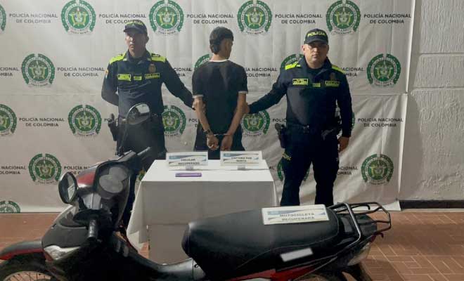 Hombre capturado en medio de dos Policías, en frente motocicleta recuperada