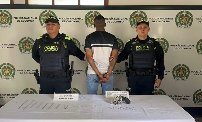 Hombre capturado en medio de dos polic&iacute;as, en frente elementos incautados