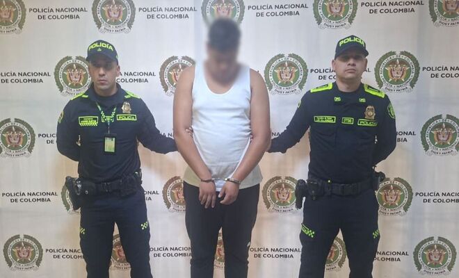 En un espacio institucional, una persona con el rostro difuminado se encuentra de pie entre dos integrantes de la Polic&iacute;a Nacional. 