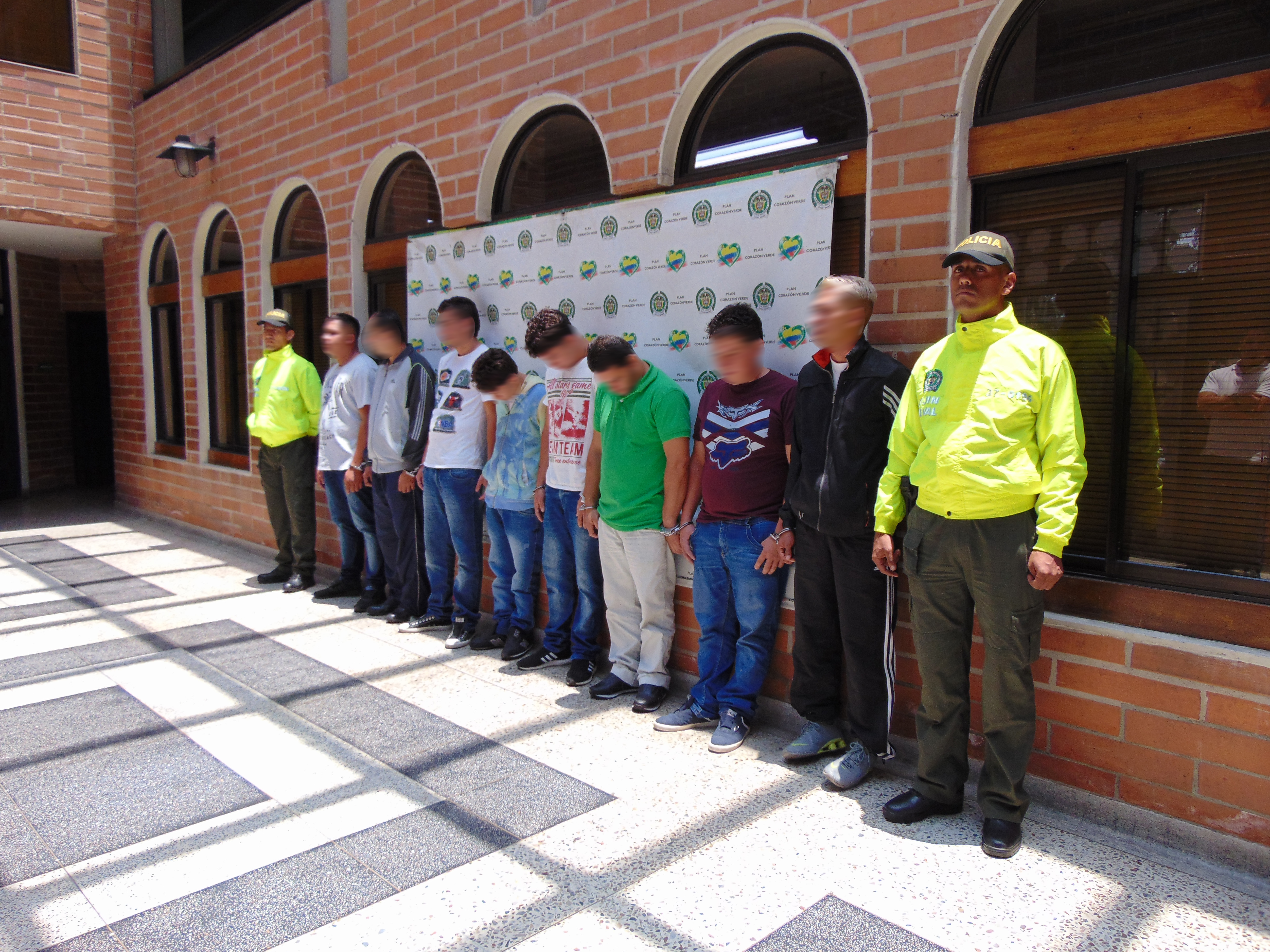 8 personas esposadas son custodiadas por dos policías de la Sijin