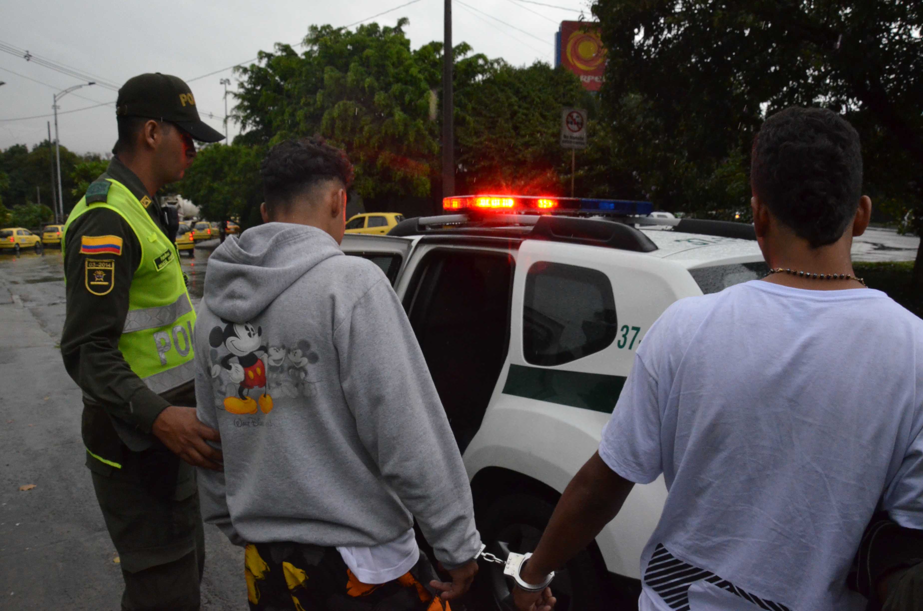 Policía lleva dos hombres hacia una patrulla luego de ser capturados por hurto