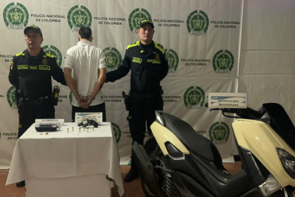 Hombre capturado en medio de dos policías, en frente elementos incautados