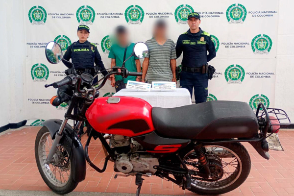 Hombres capturados en medio de dos policías, en frente motocicleta recuperada