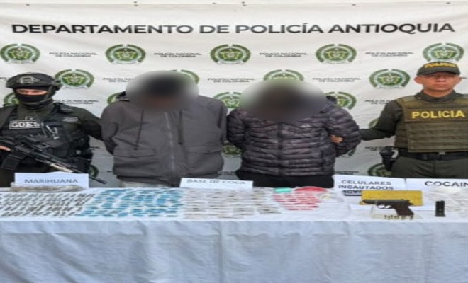 Dos policías uniformados custodian a dos capturados con estupefacientes y armas incautadas