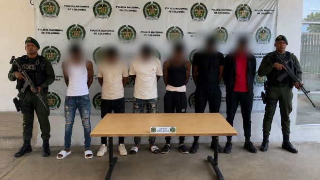 dos policías al lado de seis personas capturadas