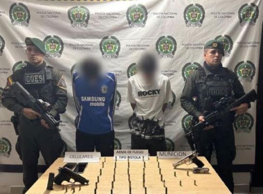 la polic&iacute;a nacional al lado de dos hombres capturados con arma de fuego y municiones 