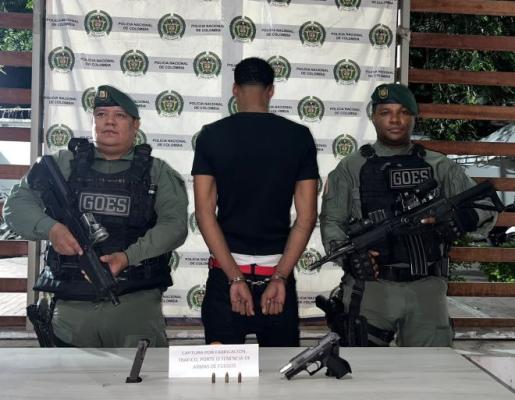 dos polic&iacute;as al lado de un hombre capturado con arma de fuego