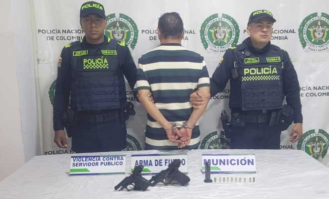 Hombre capturado en medio de dos Polic&iacute;as, en frente armas incautadas