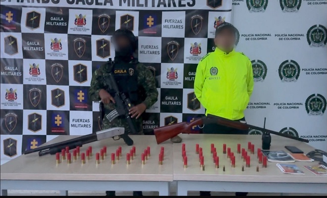 Policía y militar frente a una mesa con dos armas de fuego tipo escopetas y munición 