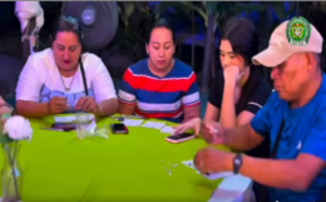 Cuatro personas sosteniendo tarjetones de bingo en una mesa con un mantel de color verde limón 