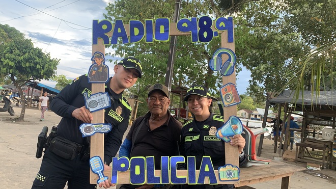 En zona rural, efectivos de la Policía posan con un habitante local junto al marco temático de la emisora, fortaleciendo lazos de confianza y difundiendo mensajes de seguridad y convivencia