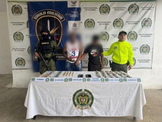 un polic&iacute;a y GAULA militar al lado de dos hombres capturados con municiones estupefacientes celulares